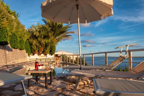 a patio with tables and an umbrella next to the water at Wonderful villa with swimming pool overlooking the sea, 200 steps from the road in Conca dei Marini