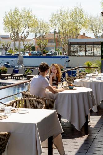 a man and woman sitting at tables at a restaurant at Hotel Port Salins by Pierre & Vacances in Empuriabrava