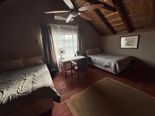 a bedroom with two beds and a desk and a ceiling fan at Kudu's Corner in Marloth Park