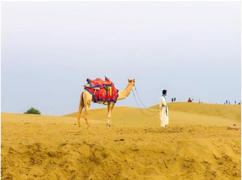 a man walking a camel in the desert at The Desert Gateway Resort in Jaisalmer