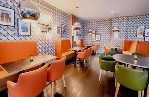 a restaurant with orange and green chairs and tables at Leonardo Hotel Wolfsburg City Center in Wolfsburg