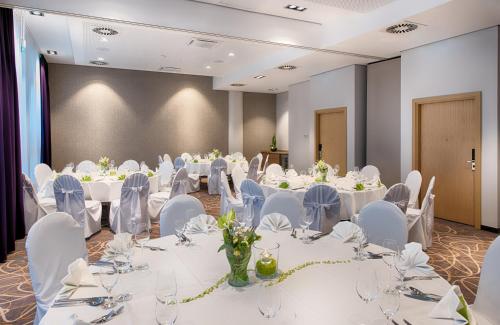 a conference room with white tables and white chairs at Leonardo Hotel Wolfsburg City Center in Wolfsburg
