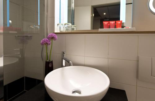 a bathroom with a sink and a vase with purple flowers at Leonardo Hotel Munich City Olympiapark in Munich