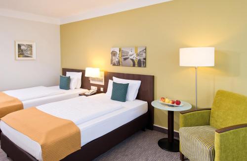 a hotel room with two beds and a chair at Leonardo Hotel Heidelberg Walldorf in Walldorf