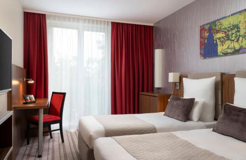 a hotel room with two beds and a desk and a window at Leonardo Hotel Dresden Altstadt in Dresden
