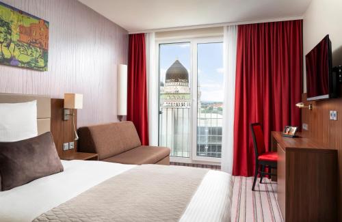 a hotel room with a bed and a desk and a window at Leonardo Hotel Dresden Altstadt in Dresden