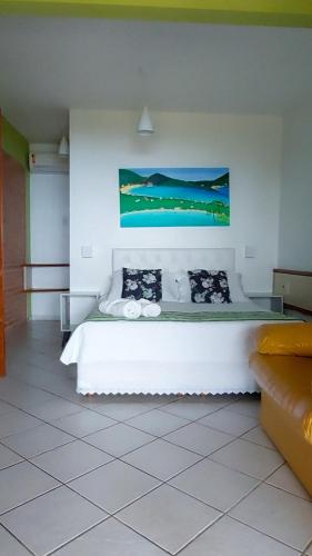 a bedroom with a white bed with a painting on the wall at Pousada Palmeiras Bombinhas in Bombinhas