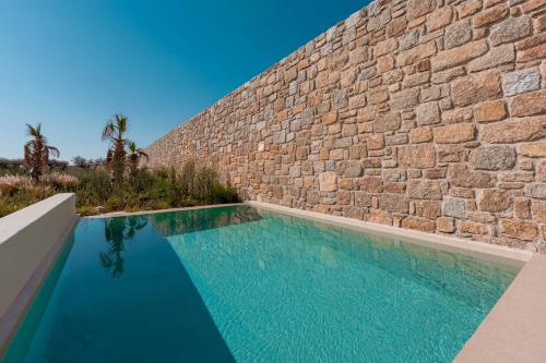 a swimming pool in front of a brick wall at Muse οf Mykonos Luxury Suites in Mýkonos City