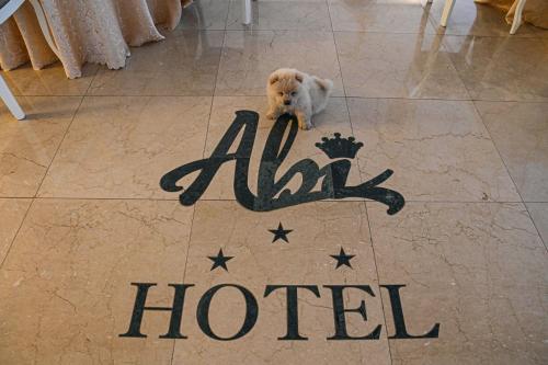 a white dog sitting on a tile floor with a hotel sign at Hotel Abyi in Baile Felix