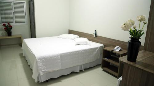 a bedroom with a white bed and a vase with flowers at Tezla Hotel in Primavera do Leste