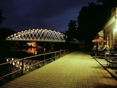 a bridge over a river with people sitting on a sidewalk at Penzion Pod Skalou in Bechyně