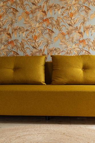 a yellow couch with two pillows in front of a wall at B&B Maas en Heuvel Maastricht in Maastricht