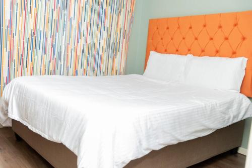 a bed with white sheets and an orange headboard at Chic and Secure Phakalane Stay in Gaborone