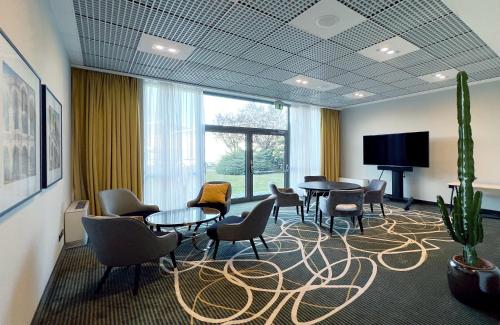 a waiting room with tables and chairs and a flat screen tv at Leonardo Hotel Verona in Verona