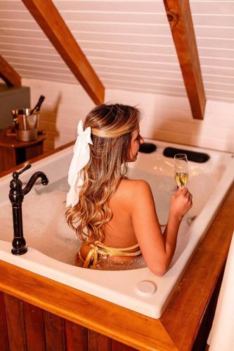 a woman sitting in a bath tub holding a glass of wine at Chalé cruzeiro do sul, hidromassagem, 2 min Thermas Machadinho-RS #2 in Machadinho