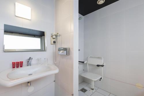 a white bathroom with a sink and a toilet at Leonardo Hotel Almere City Center in Almere