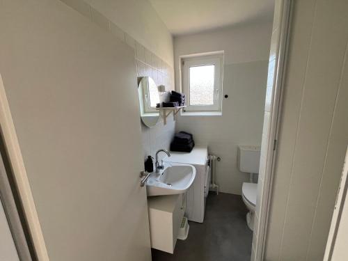 a white bathroom with a sink and a toilet at Vier Nordlichter Erdgeschosswohnung mit Terrasse und Garten in Bensersiel