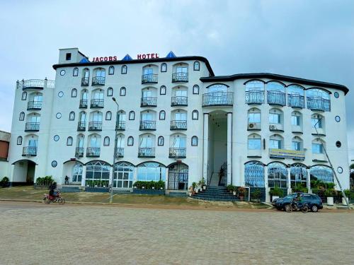 a large white building with cars parked in front of it at Jacobs Hôtel in Douala