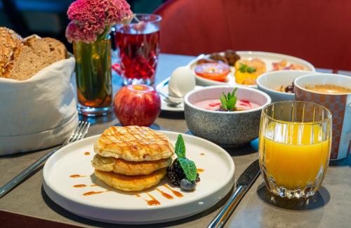 a table with a plate of pancakes and a glass of orange juice at Leonardo Royal Hotel Nürnberg in Nuremberg