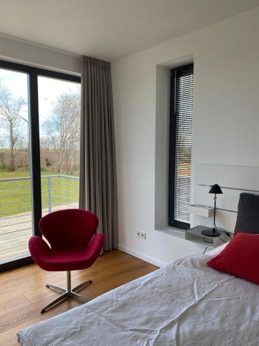 a bedroom with a red chair and a large window at Haus Charly Exklusives Architektenhaus Holzbauweise Fehmarn, strandnah in Fehmarn