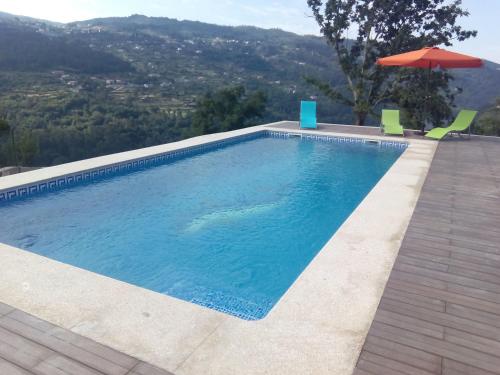 a swimming pool with two chairs and an umbrella at Casa do Alto in Magrelos