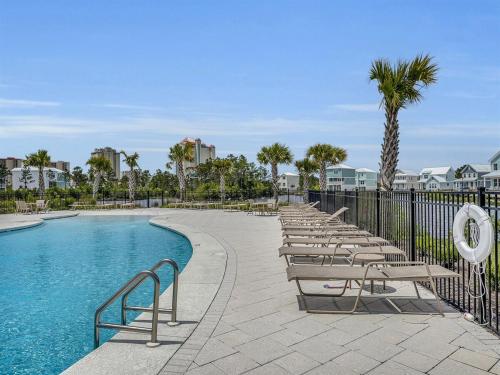 a pool with chairs and a fence and palm trees at Coastal Bummz in Orange Beach