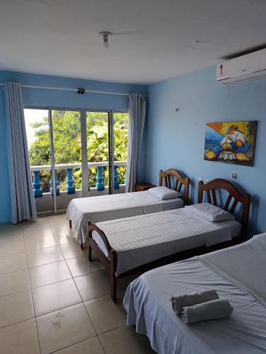 a room with three beds and a window with a view at Pousada Azul da Broadway in Canoa Quebrada