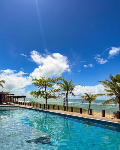a swimming pool next to a beach with palm trees at Hotel Espelho D'Água Arraial e Beach Club in Arraial d'Ajuda