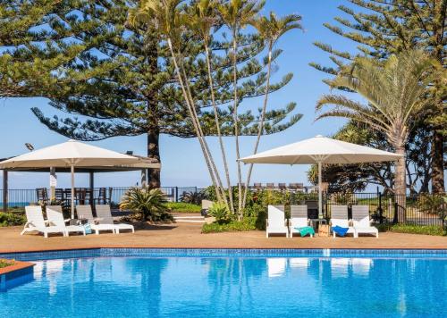 a swimming pool with chairs and umbrellas at Nautilus Beach Apartment 109 in Coffs Harbour