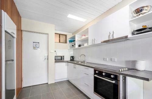 a kitchen with white cabinets and a black appliance at Nautilus Beach Apartment 109 in Coffs Harbour