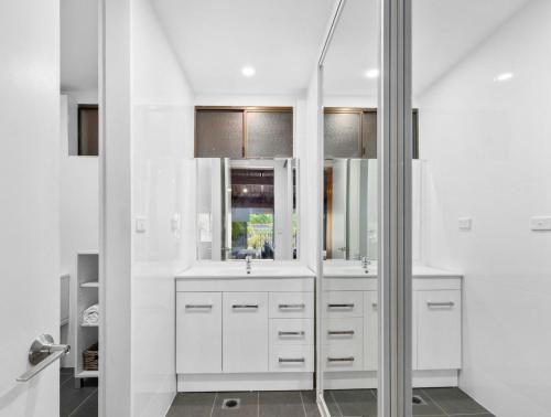 a white bathroom with two sinks and a mirror at Nautilus Beach Apartment 109 in Coffs Harbour