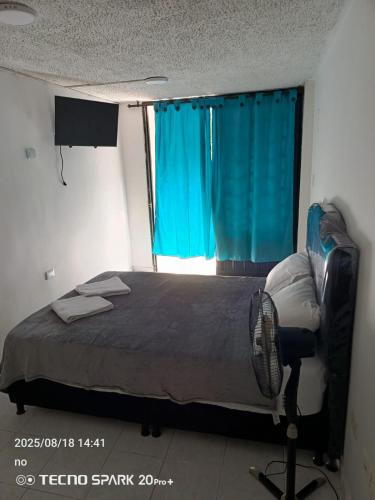 a bedroom with a bed and a window with blue curtains at Hotel Kenisoni in Ibagué