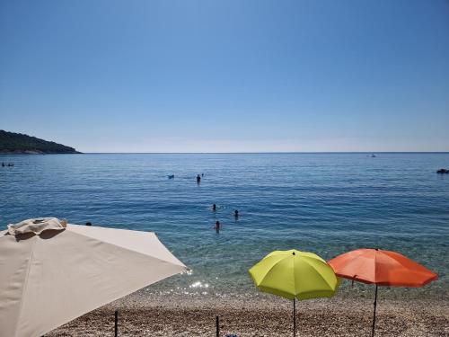 two umbrellas on a beach with people in the water at Lovely Home by the Beach in Kruče
