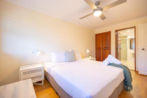 a bedroom with a large white bed and a fan at Surfrider - Beach front apartment with pool in Byron Bay