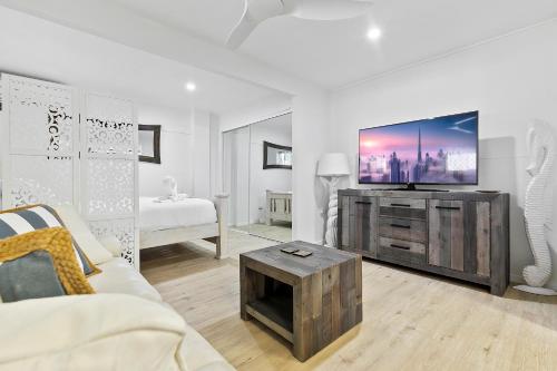 Una sala de estar con un televisor de pantalla plana en un centro de entretenimiento. en Funky Lil Shack - by the jetty, en Bongaree