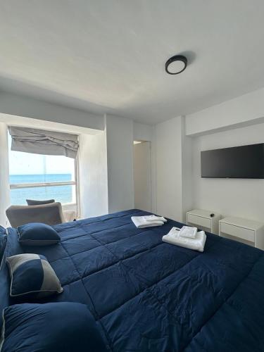 un grande letto blu in una stanza con finestra di Apartamento de lujo frente al mar en residencia con piscina, planta electrica y gym a Porlamar