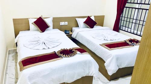 two beds in a room with white sheets and red pillows at Hotel Kavya International in Bharatpur