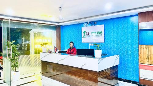 a woman standing at a reception desk in a blue room at Hotel Kavya International in Bharatpur