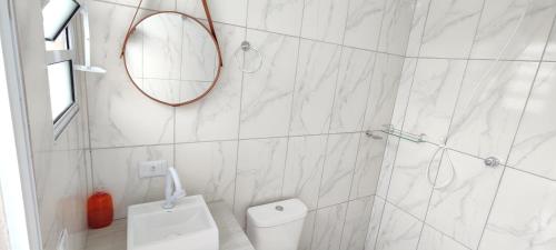 La salle de bains blanche est pourvue d'un miroir et de toilettes. dans l'établissement Casa térrea com piscina a 250 metros da praia, à Itanhaém