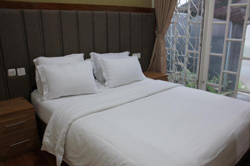 a white bed with white pillows and a window at Diyar Villas Puncak M3/47 in Puncak