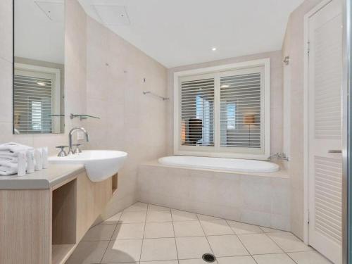 a white bathroom with a tub and a sink at The Pool Resort Kingscliff - Private Apartments by Holiday Management Company in Kingscliff