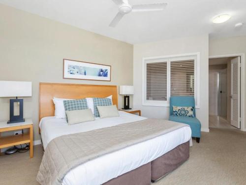 a bedroom with a large bed and a blue chair at The Pool Resort Kingscliff - Private Apartments by Holiday Management Company in Kingscliff