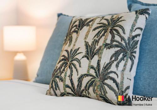 a pillow with palm trees on it sitting on a bed at River & Reef Retreat in Iluka