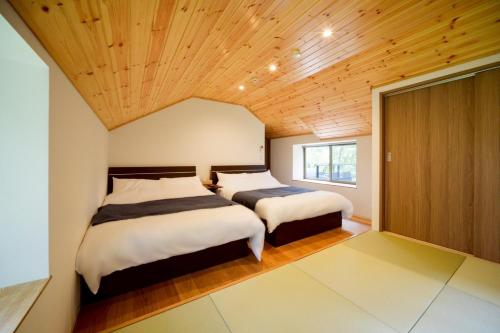 two beds in a bedroom with a wooden ceiling at GRACE VILLA Aso Kurokawa in Minamioguni