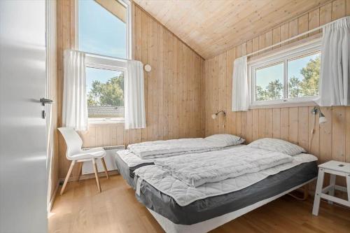 a bedroom with a bed and a chair and two windows at 1563-Aakirkeby-Strandparken-8 in Vester Sømarken