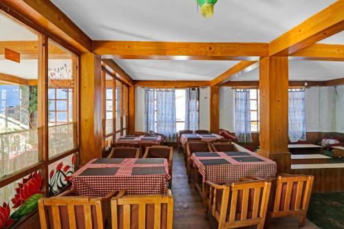 a row of tables and chairs in a room with windows at Capital O Himalayan Travels in Manāli