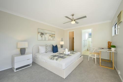 a white bedroom with a bed and a desk at Stunning 4BR Home with Pool & Water Views in Koolewong
