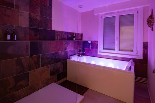 a bathroom with a tub and a window with purple lighting at L'Escapade Secrète balnéo - sauna - love room in Arras