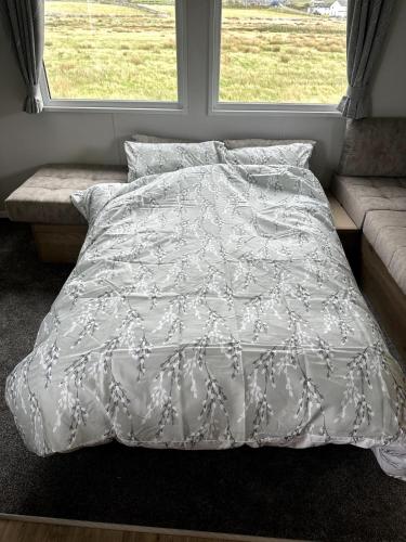 a bed with a white comforter and two windows at Luxury static caravan on SunnySands with mountain views in Barmouth
