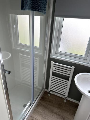 a bathroom with a shower and a sink and two windows at Luxury static caravan on SunnySands with mountain views in Barmouth